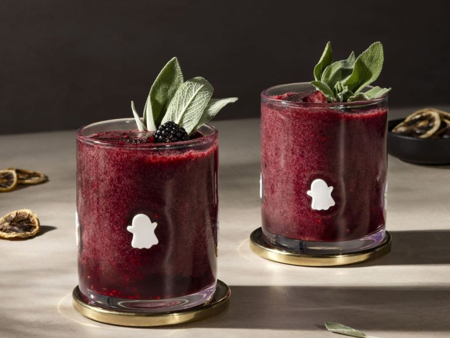 two glass cups with white ghosts on them and a sprig of mint 