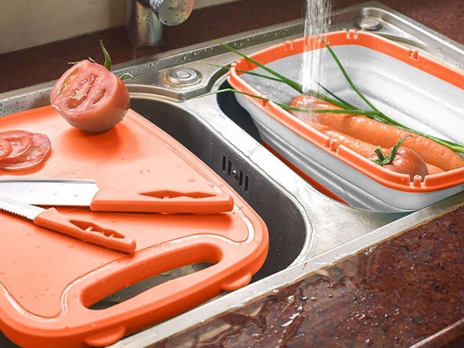 An orange cutting board with various kitchen tools on kitchen sink