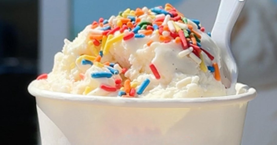 an ice cream scoop in a cup with sprinkles and a spoon