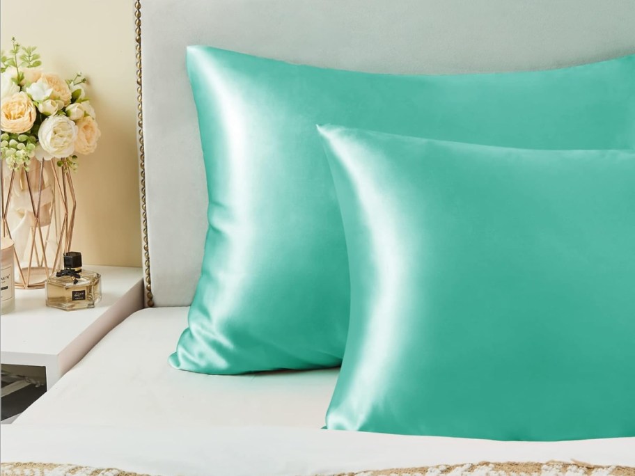 two bed pillows in green satin pillowcases on a bed