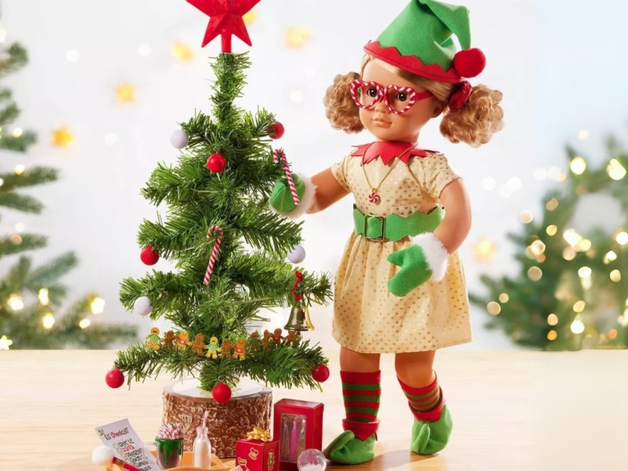 a doll wearing a Christmas elf outfit next to a small tree