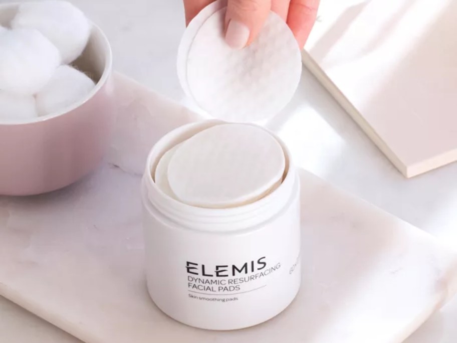 hand pulling a facial cleansing pad out of a container