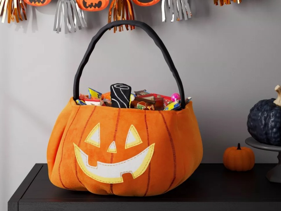 a large Jackolantern trick or treat basket on a table with Halloween decor