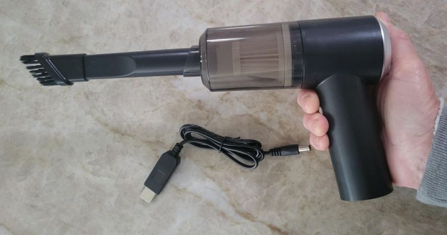 Hand holding a mini portable vacuum with a brush attachment on it