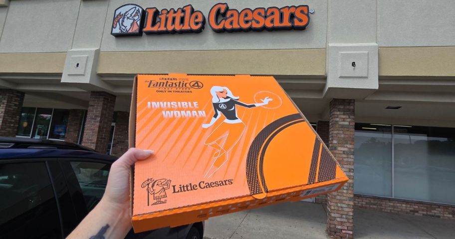 Hand holding up a Fantastic 4 Pizza Box in front of a Little Caesar's store