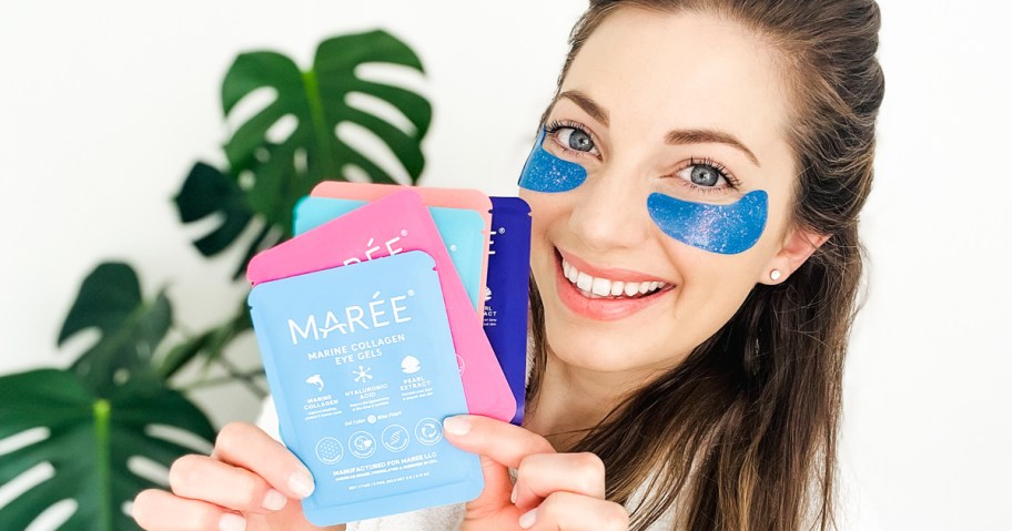 woman holding up multiple packs of eye gels while wearing a blue pair under her eyes