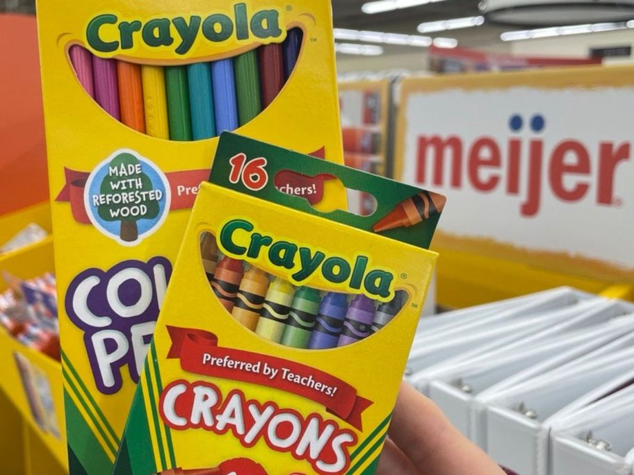 Hand holding up boces of Crayola Colored Pencils and crayons in front of a meijer sign