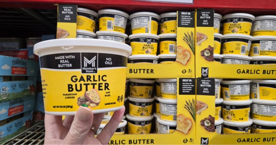 A person holding a Member's Mark Garlic Butter tub in front of a fridge full of the same