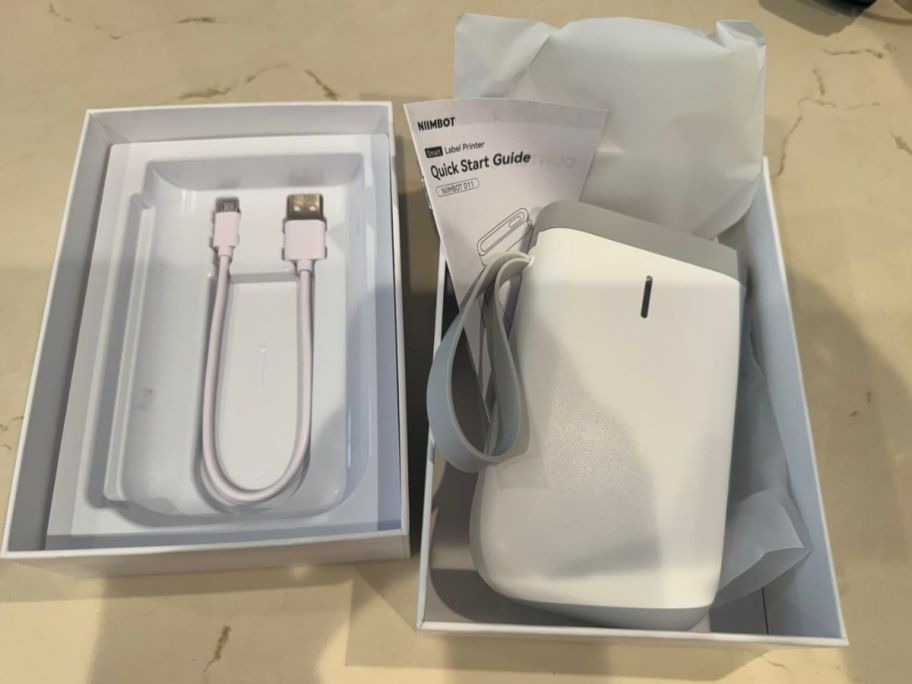 A white label maker in a box with its charger beside it 