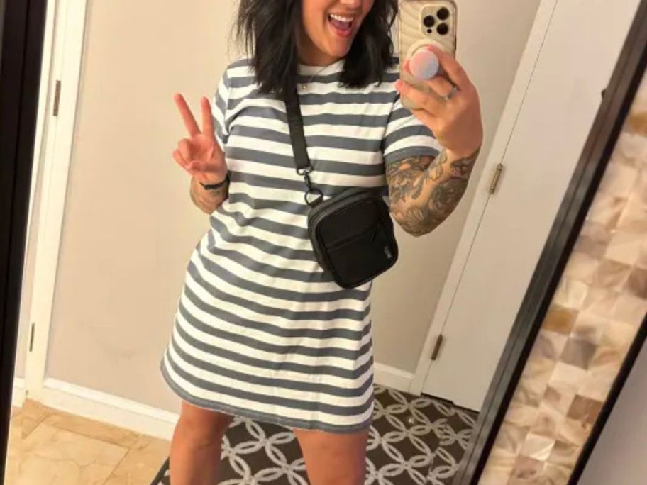 A woman wearing a striped gray and white dress flashing the peace sign 