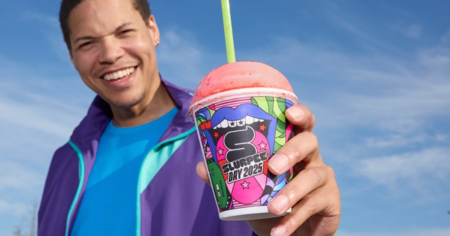 Man holding small 711 Slurpee with green straw and standing outside