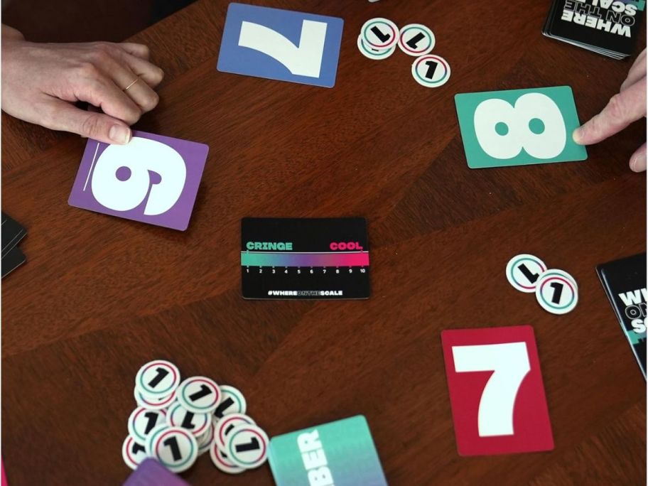 A table with Spin Master Where on The Scale Adult Party Game cards and game pieces