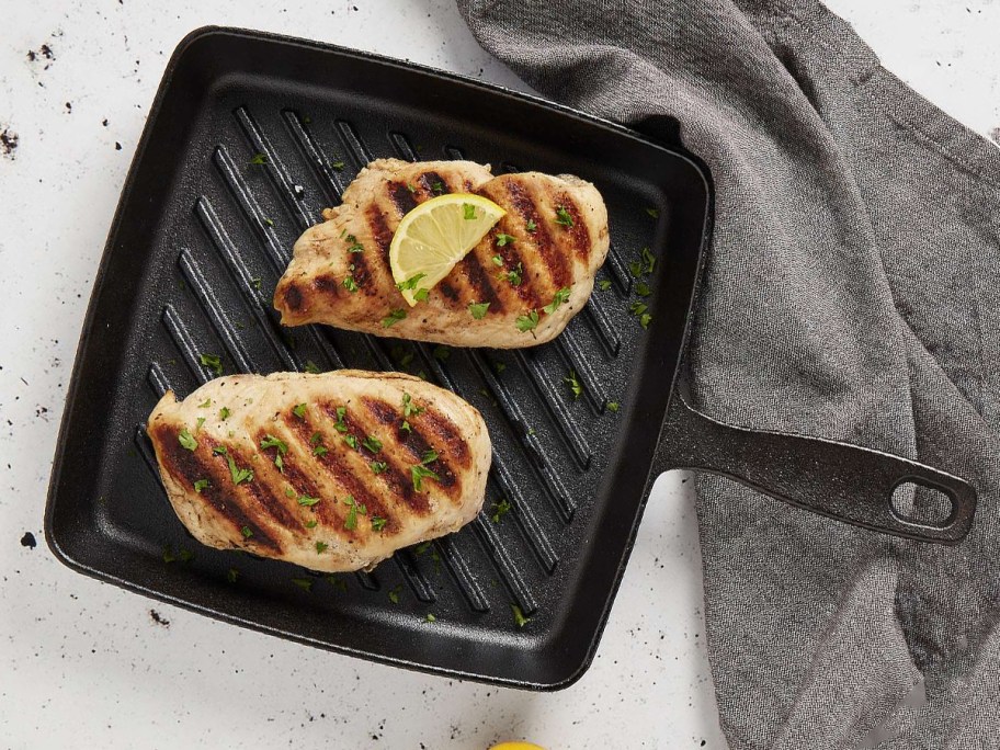 The Big One 9.8in Pre-Seasoned Cast-Iron Grill Pan sitting on a counter with meat in it