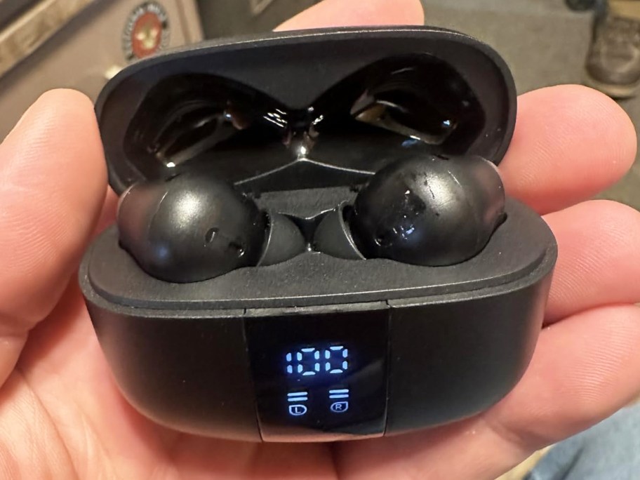 hand holding a pair of black bluetooth earbuds in charging case