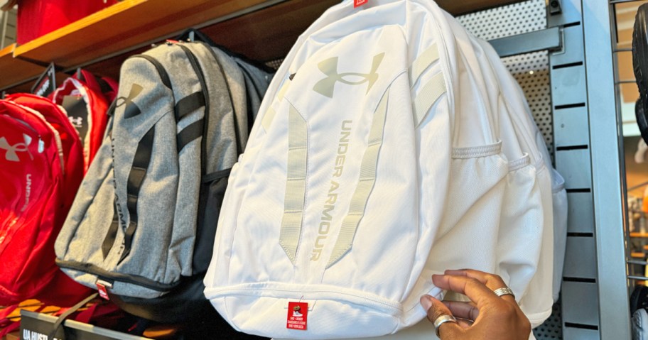 hand touching a white under armour backpack on display in store