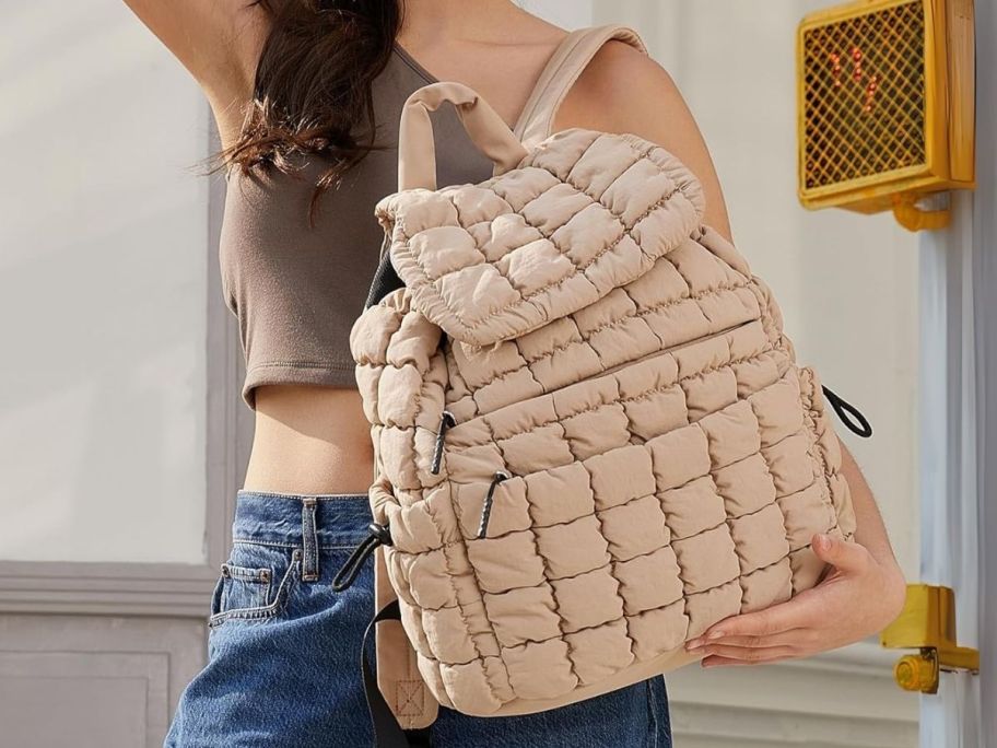 a woman holding a beige puffer backpack