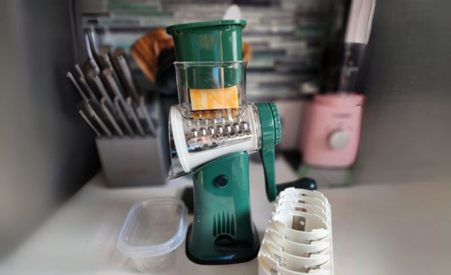 a green cheese grater shown with blades and accessories