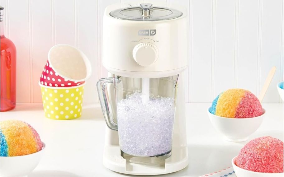 a dash shaved ice and slushie maker on a kitchen countertop shown with shaved ice treats