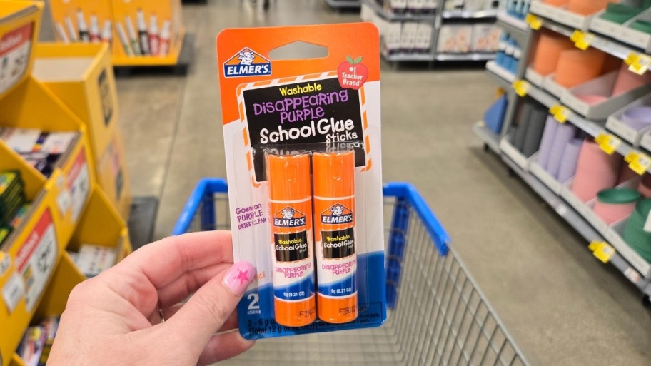 a womans hand holding a 2 pack of glue sticks