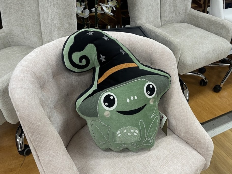 a witch frog pillow propped up in a chair in a store