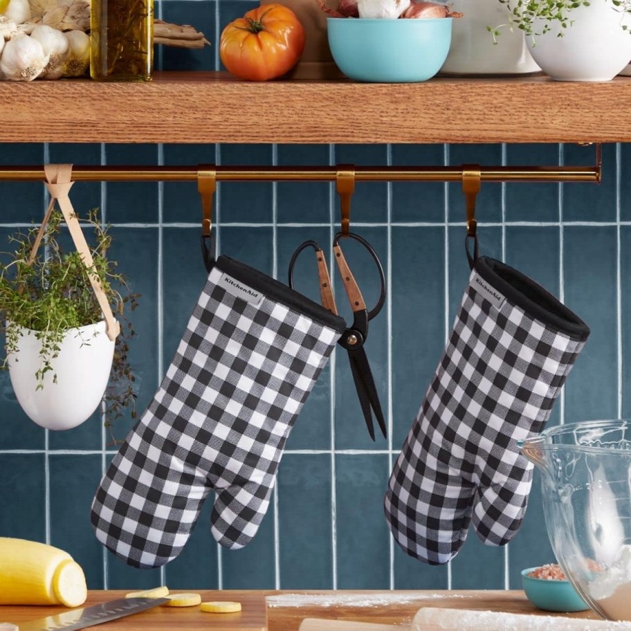 a pair of gingham oven mitts hanging from a kitchen shelf
