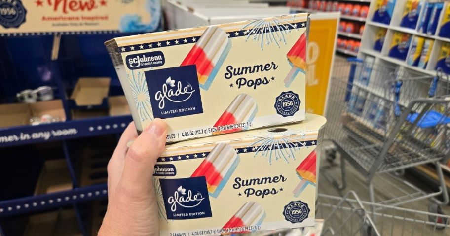 a womans hand holding two 2 packs of scented candles