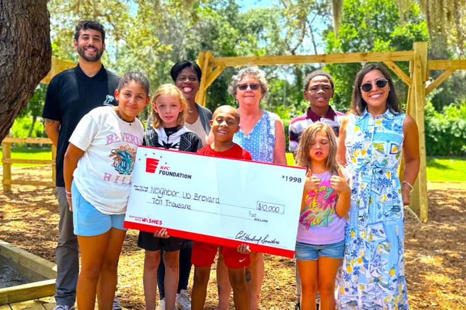 kids and adults standing behind big KFC donation check
