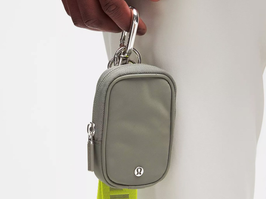 person holding a small grey zippered pouch with clip at the top