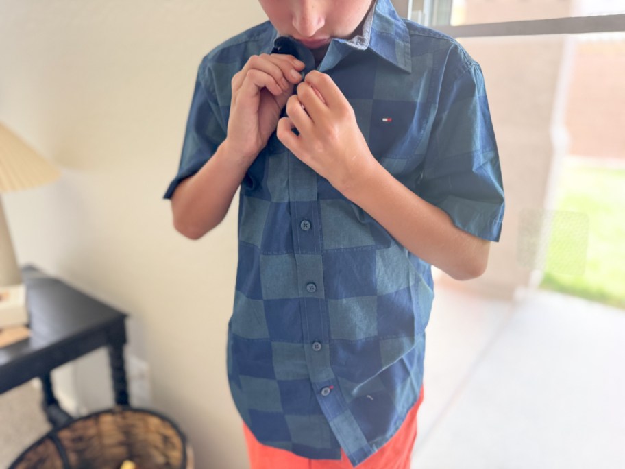 boy buttoning blue checked shirt
