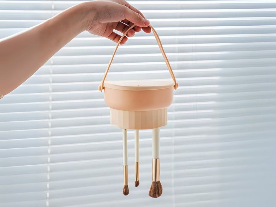 hand holding makeup brush cleaner bowl upside down with brushes hanging from it