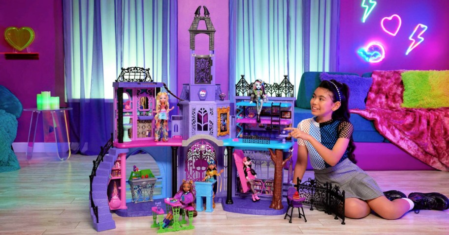 girl sitting next to a monster high doll house
