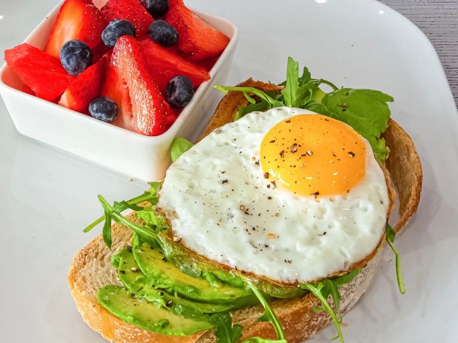 round egg on sandwich next to bowl of berries