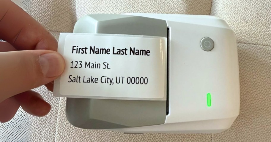 a hand pulling a label off a small wireless label maker