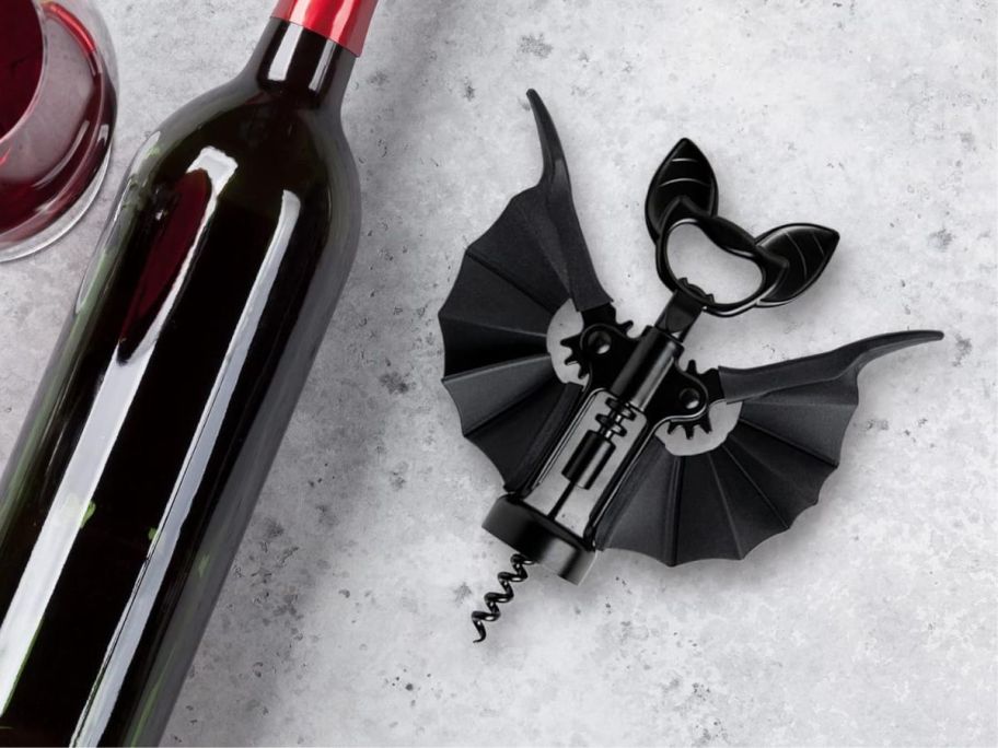 OTOTO Bat 2-in-1 Wine & Beer Opener laying next to wine bottle