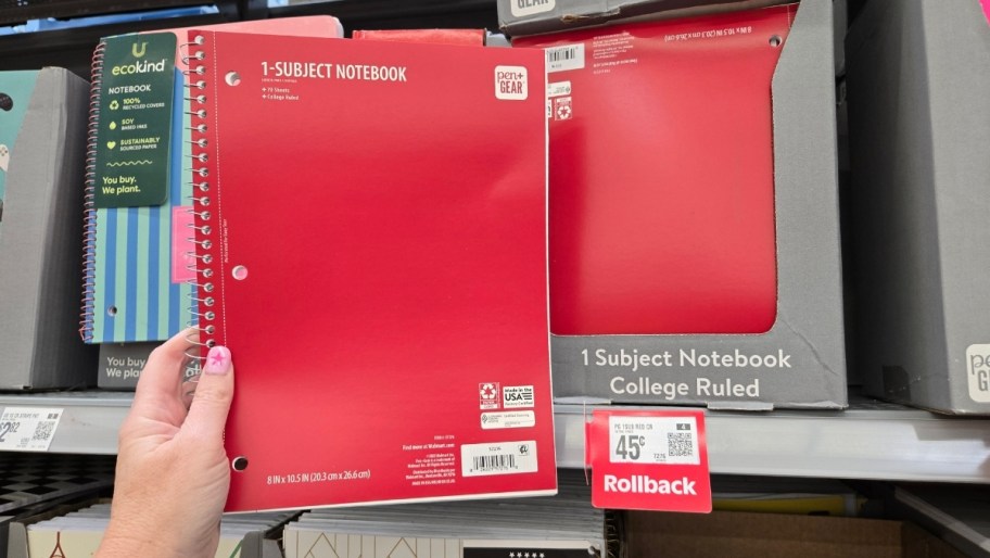 a womans hand holding ared one subject spiral notebook