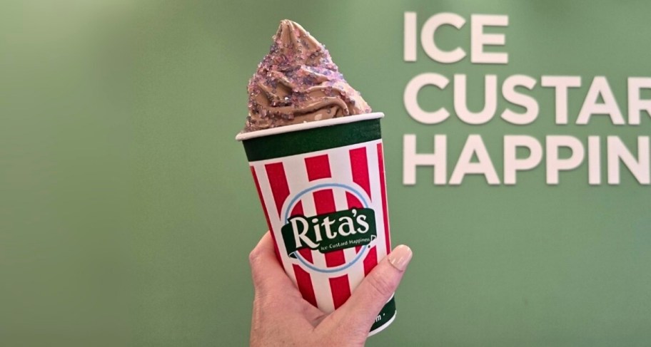 a womans hand holding a cup of gelati with unicorn glitter sprinkles on top