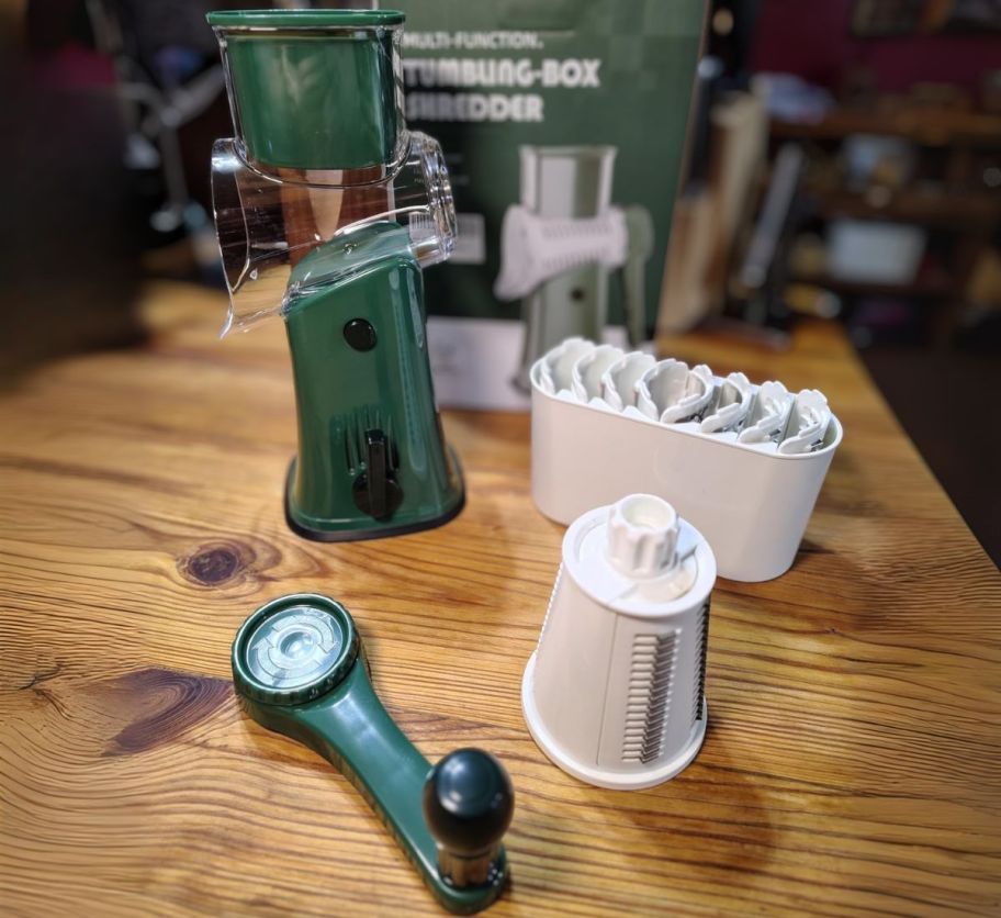 a green rotary cheese grater shown with blades and accessories