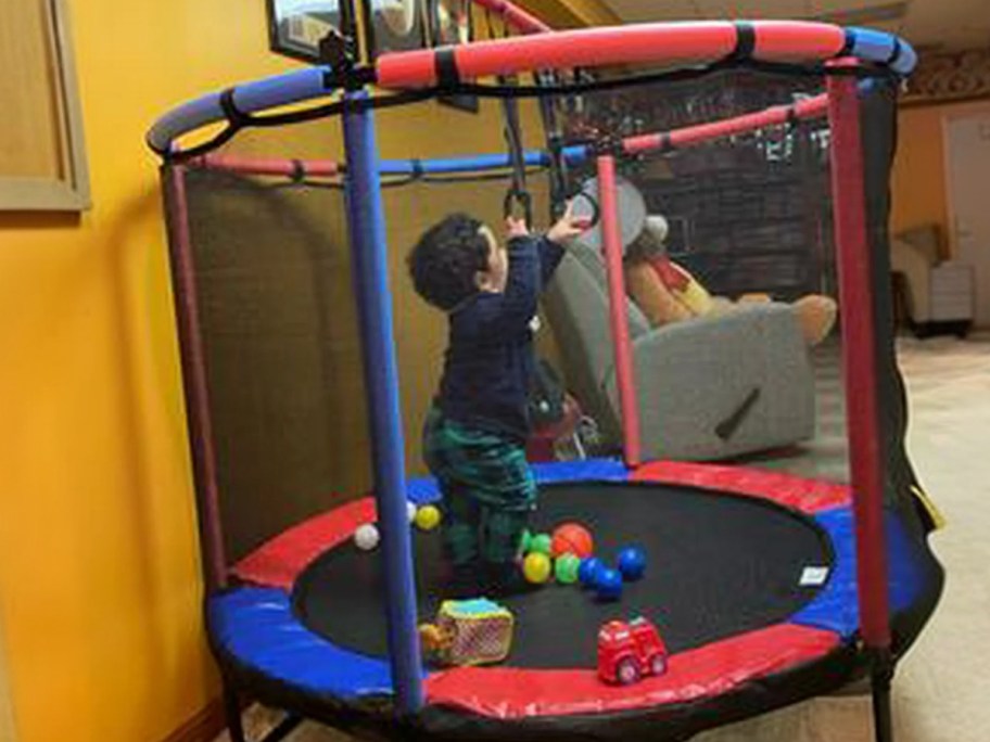 little boy playing in a toddler trampoline with safety net and toys