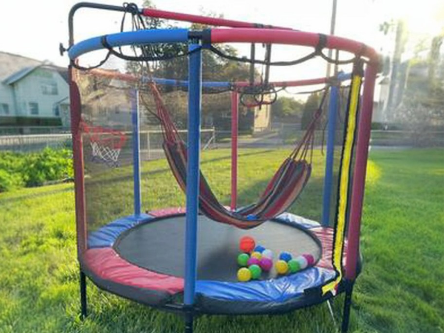 a kids small trampoline with safety net, swing, and basketball hoop in a backyard