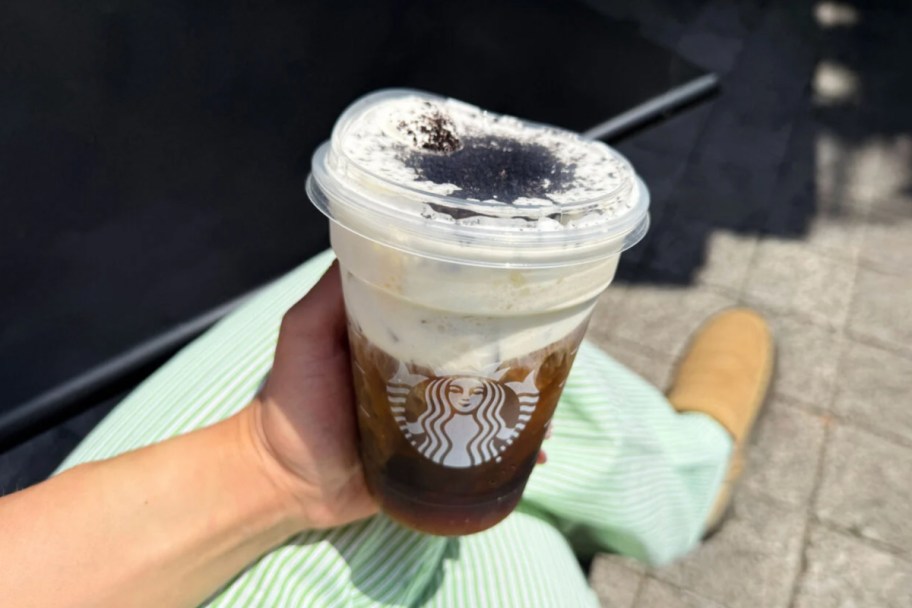 hand holding cookies and cream drink over green pants