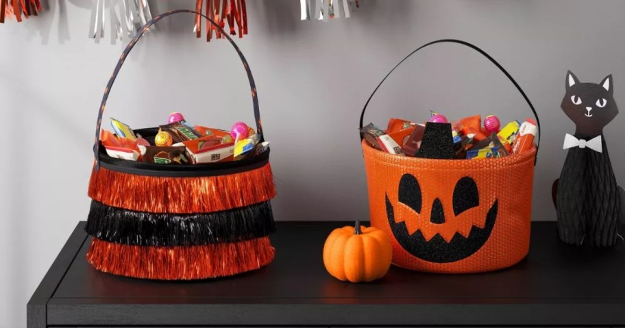 a black and orange tinsel and a sequin pumpkin trick or treat baskets on a table with Halloween decor