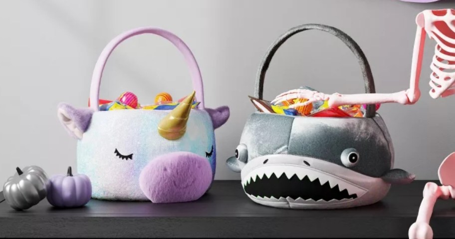 a unicorn and a shark trick or treat baskets on a table with Halloween decor
