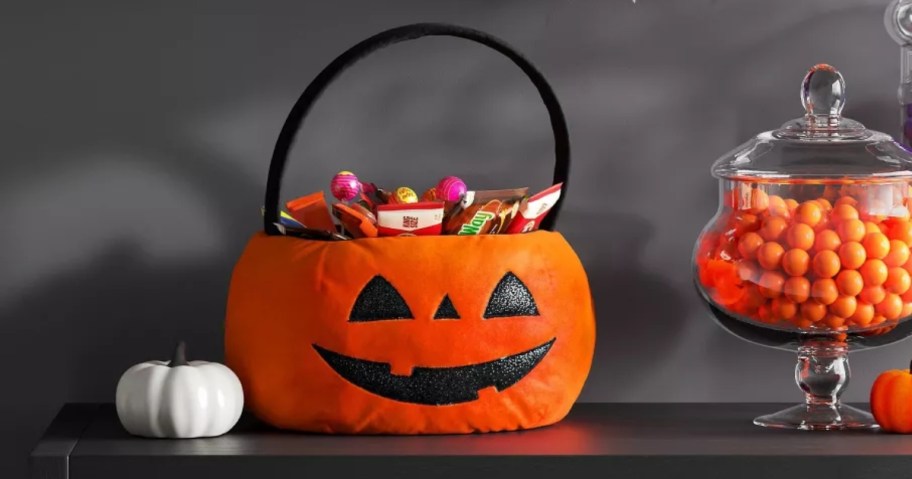 a fabric pumpkin trick or treat basket on a table with Halloween decor