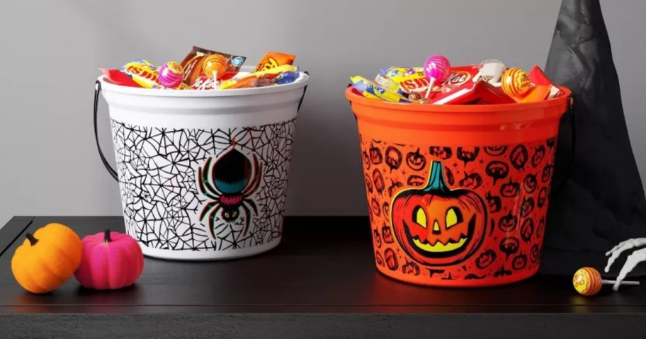 2 plastic trick or treat buckets on a table with Halloween decor