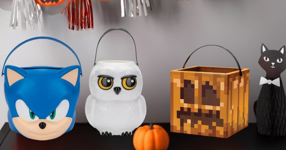 three trick or treat pails on a table with Halloween decor - Sonic the Hedgehog, Hedwig from Harry Potter, and a Minecraft Jackolantern