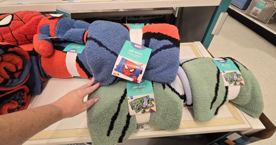 hand reaching for Marvel throw blankets on a shelf at Target