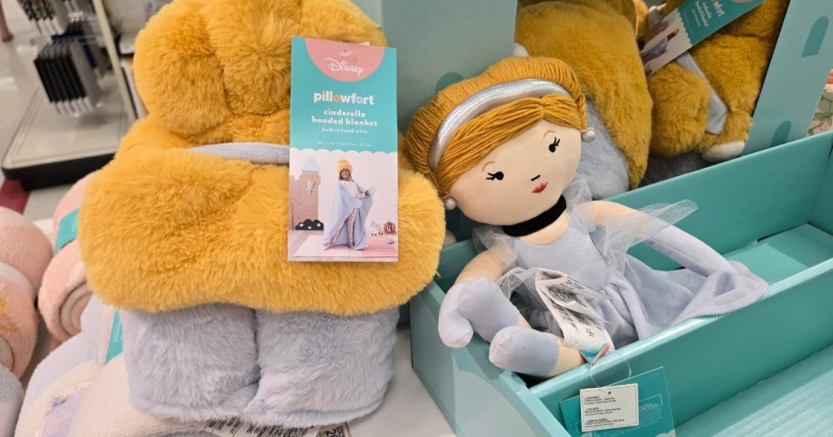 hand holding a Cinderella hooded throw blanket, a Cinderella Plush doll is next to it at Target
