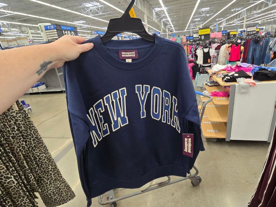 had holding Weekend Academy Girls Long-Sleeve Graphic Crewneck Sweatshirt with "new york" on it