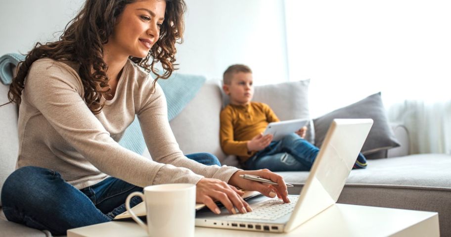 woman sitting on couch working on computer with son beside her