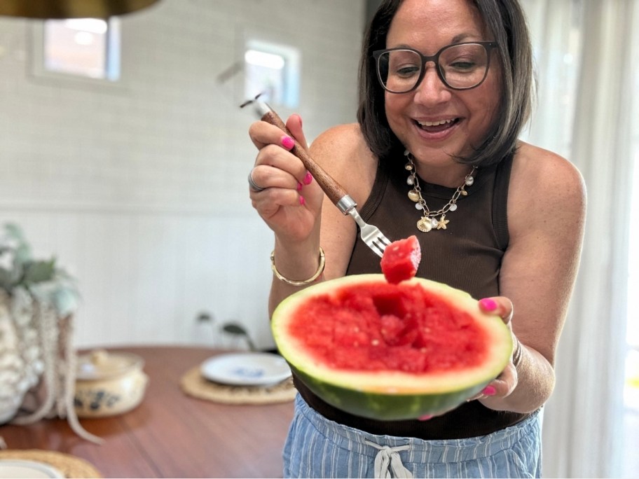a woman holding half a watermelon with one hand and a fork with the other.